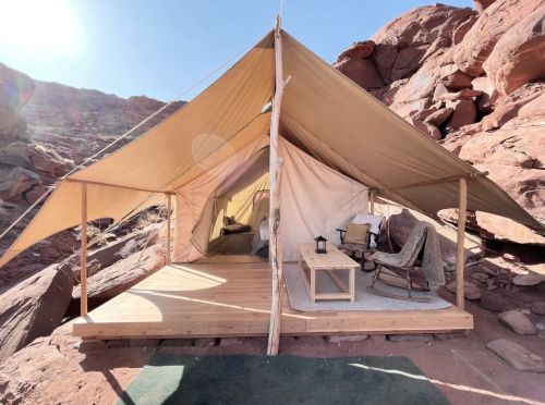 A cozy tent on a wooden deck, set against rocky terrain and clear blue skies.